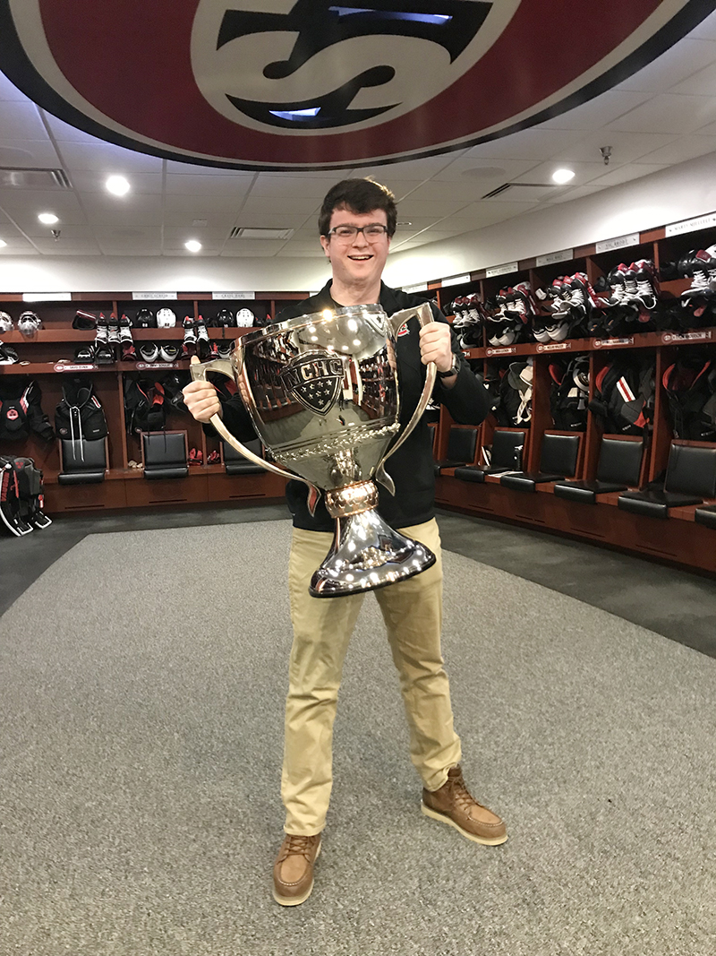 Alex Ward poses with the NCHC Cup in the St. Cloud State Men's Hockey locker room.