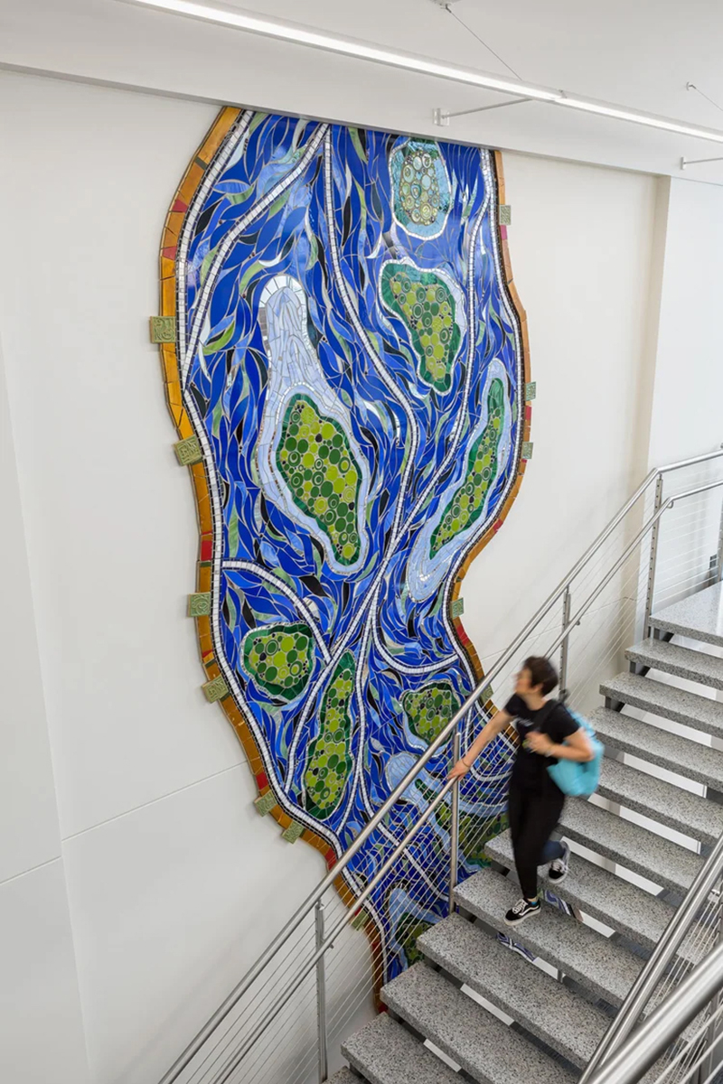 Stacia Goodman walking in front of her mosaic mural in Eastman Hall at St. Cloud State.